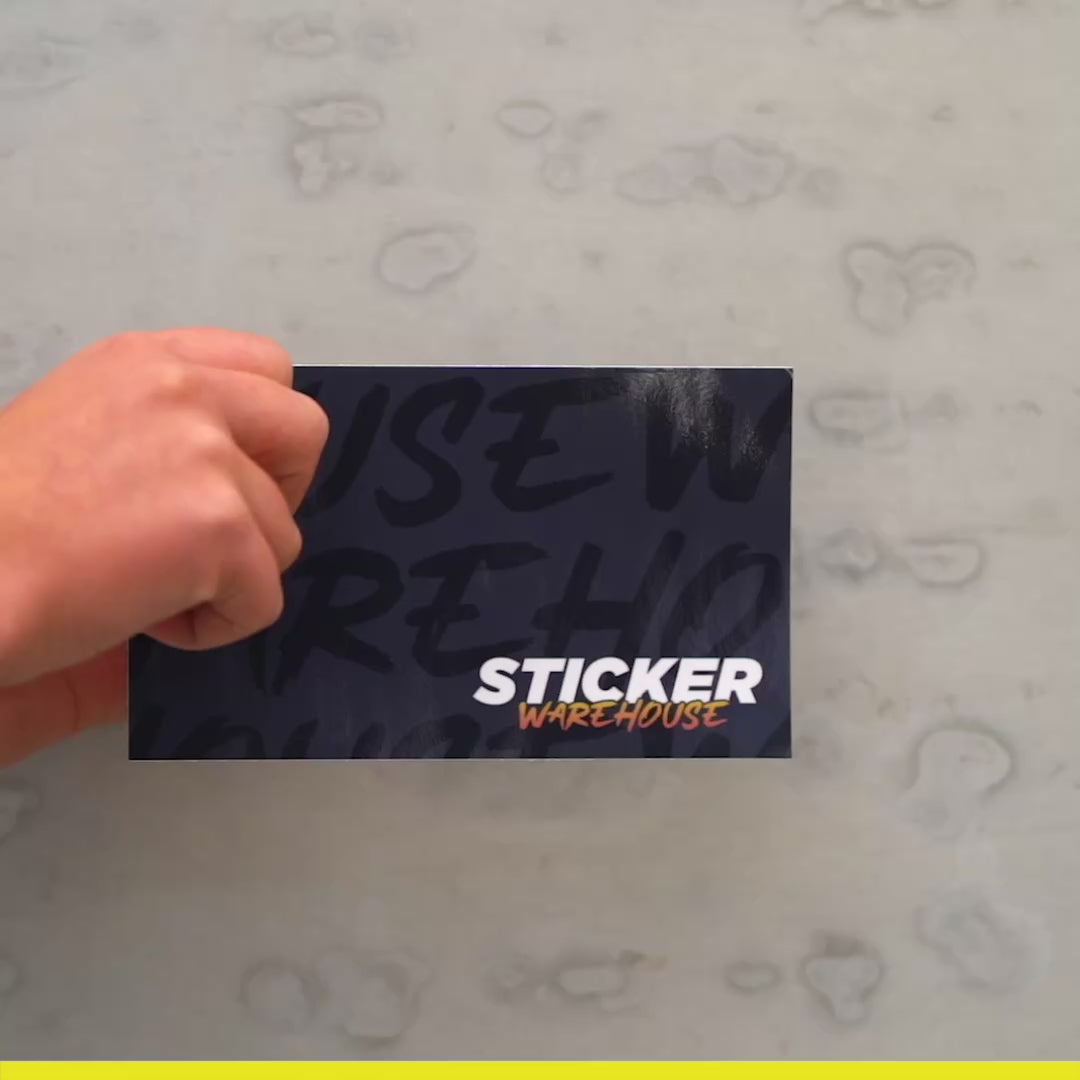 Hand holding a custom rectangle sticker from Sticker Warehouse on a textured background.